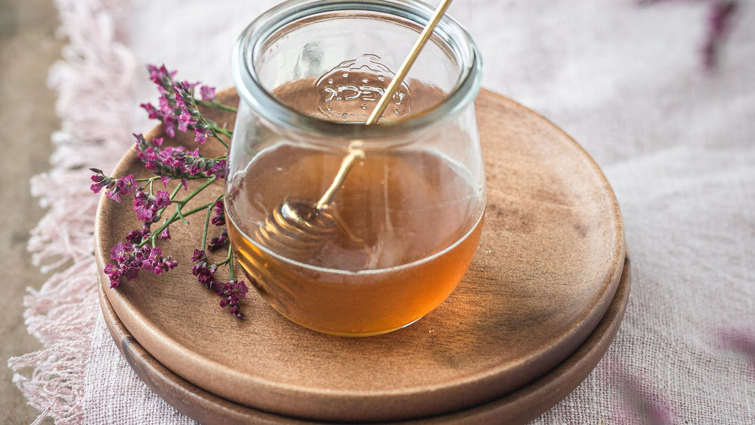 Jar of honey with a wooden dipper surrounded by wildflowers on a rustic linen cloth
