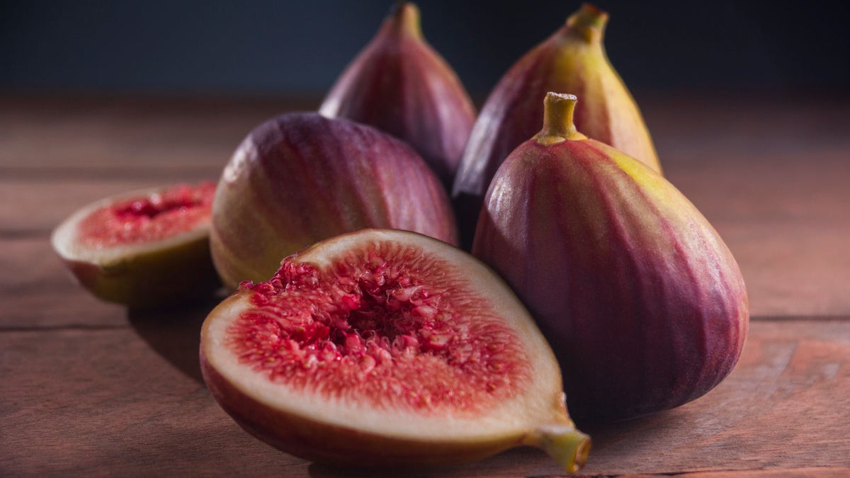 Whole and sliced ripe figs on a rustic wooden surface, showing their red interior