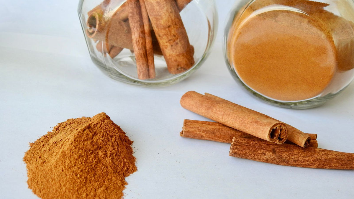 Ground cinnamon powder and cinnamon sticks in small glass jars on a white background