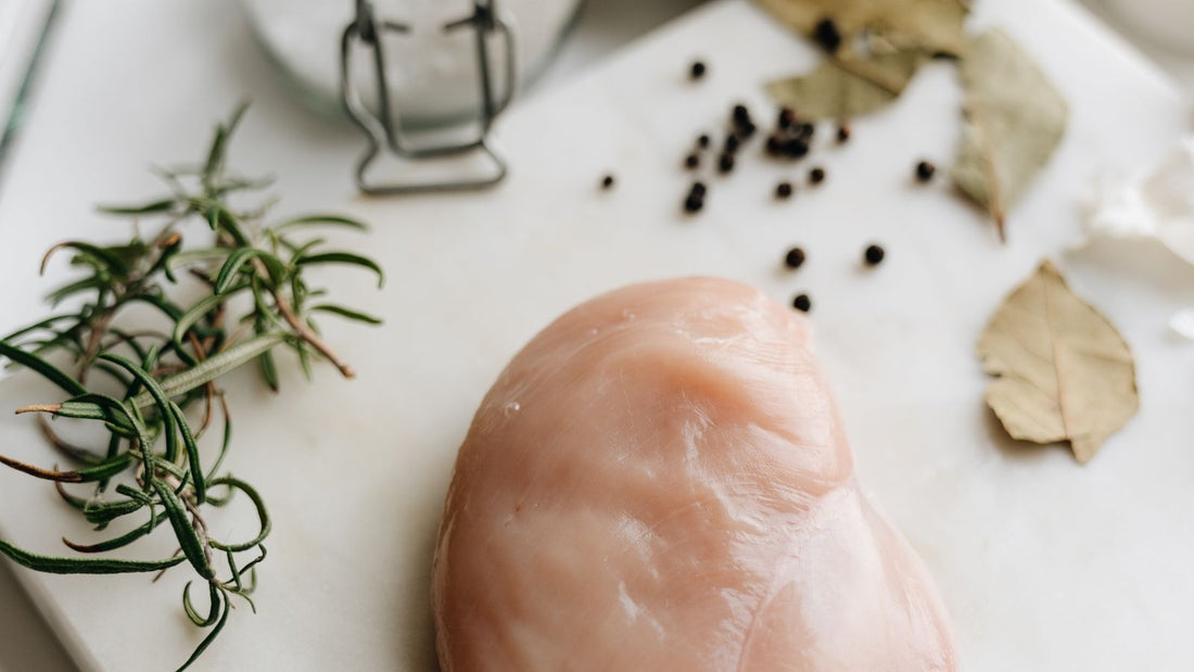 Raw chicken breast on a marble surface with fresh herbs
