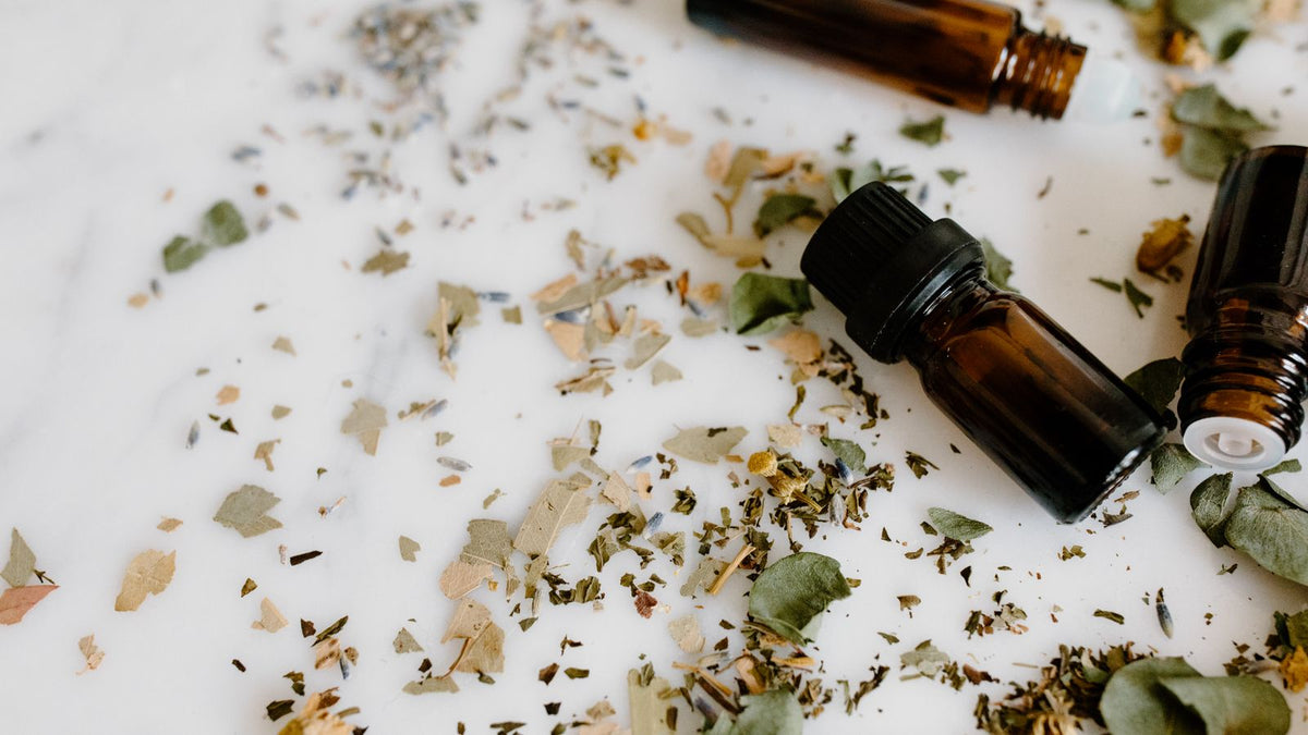 Amber glass essential oil bottles with dried herbs on a white surface